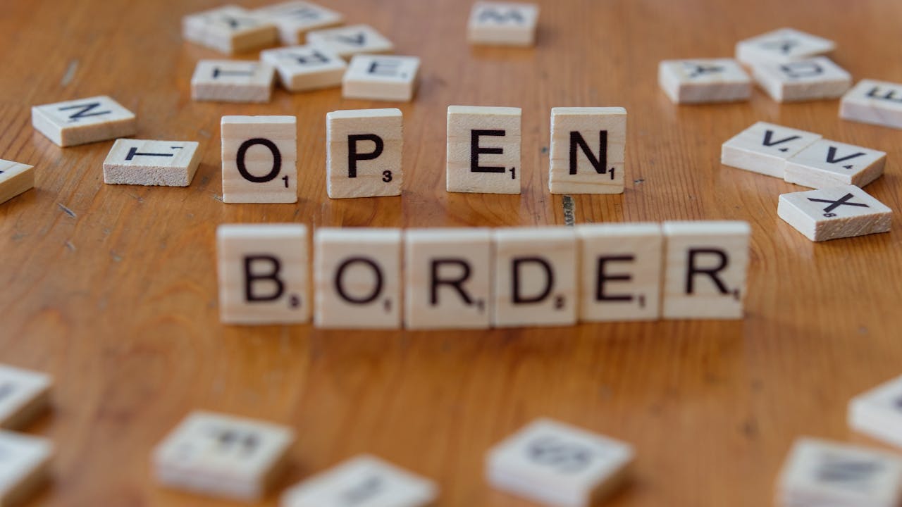 Wooden Scrabble letters on a table spelling out 'open border', concept of migration and geopolitics.